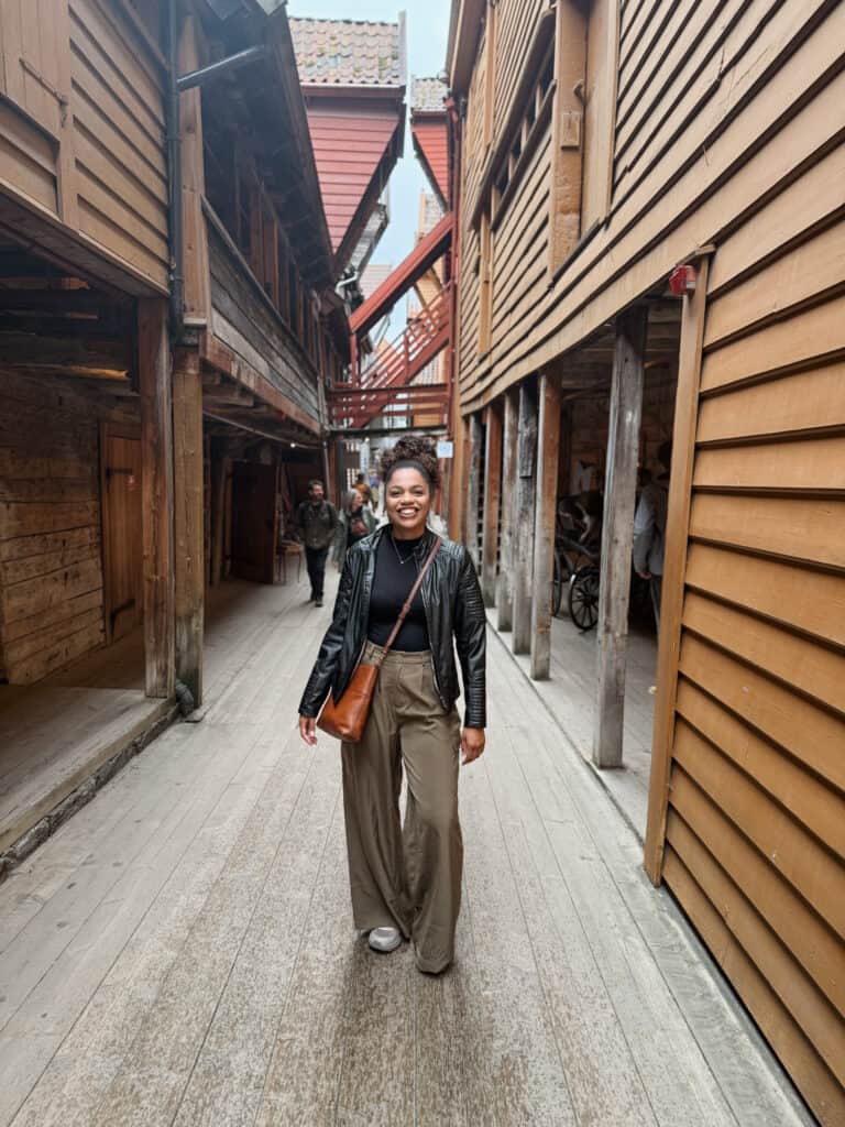 Home 13 Girl standing between two wooden buildings smiling at the camera.